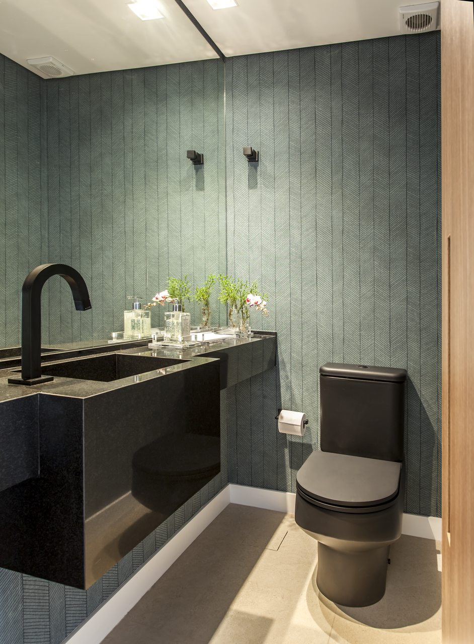 Seguindo a paleta escura, a bacia sanitária com acabamento matte, papel de parede e a bancada com cuba esculpida | Projeto de Korman Arquitetos (Foto: Eduardo Pozella)